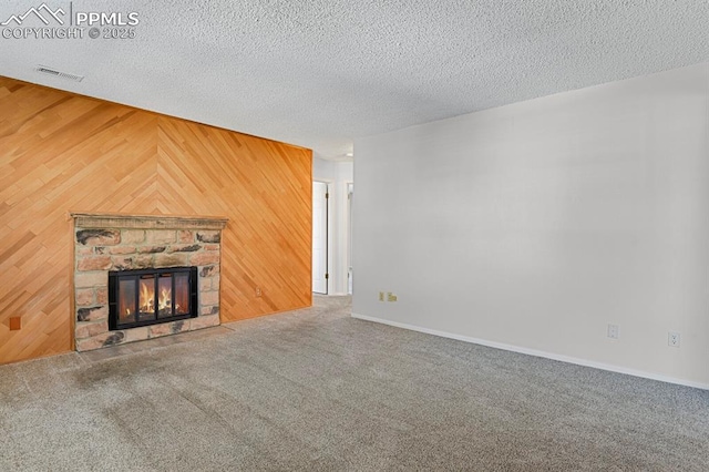 unfurnished living room featuring wooden walls, visible vents, carpet flooring, and a stone fireplace