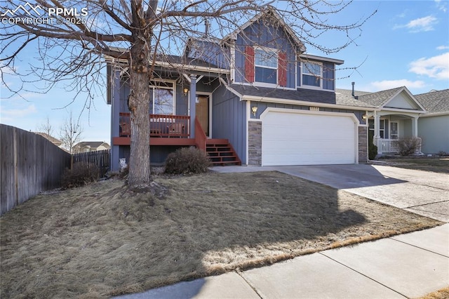 view of front facade with driveway, stone siding, an attached garage, fence, and a porch