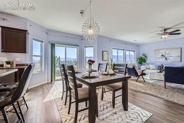 dining area with light wood-style flooring, baseboards, and ceiling fan with notable chandelier