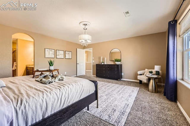 carpeted bedroom with arched walkways, visible vents, an inviting chandelier, connected bathroom, and baseboards