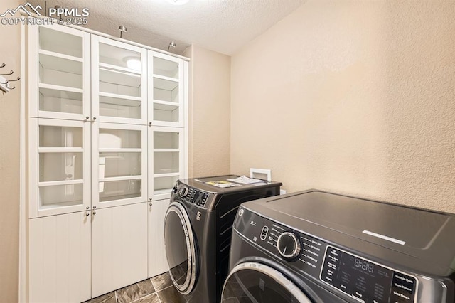 laundry area with a textured ceiling, a textured wall, separate washer and dryer, and cabinet space