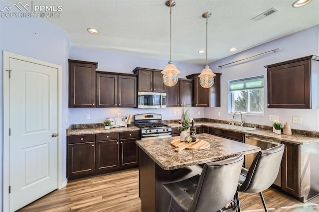 kitchen with light wood finished floors, visible vents, appliances with stainless steel finishes, a sink, and dark brown cabinetry