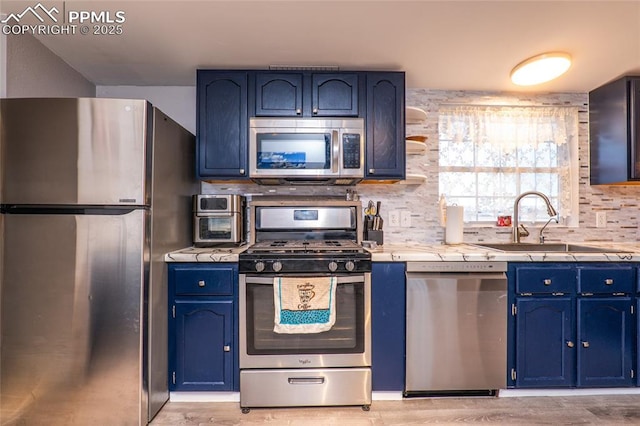 kitchen with tile counters, tasteful backsplash, appliances with stainless steel finishes, a sink, and blue cabinets