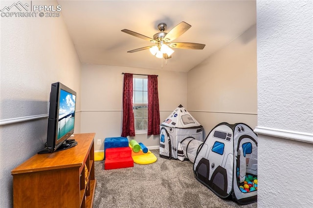 recreation room featuring a ceiling fan, carpet, and a textured wall