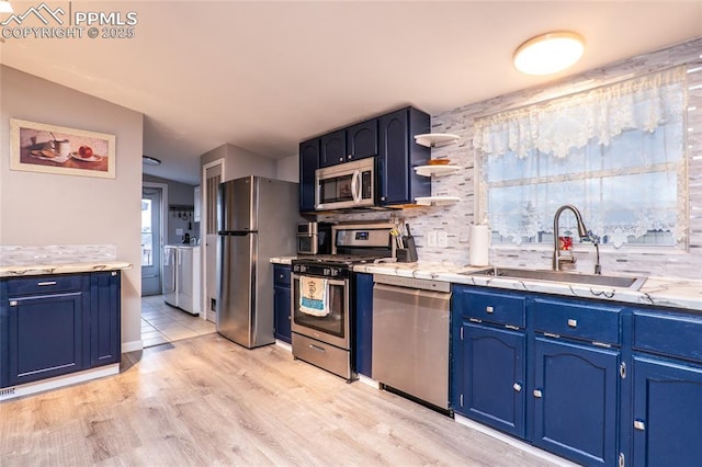 kitchen featuring light wood-style flooring, blue cabinets, stainless steel appliances, a sink, and backsplash