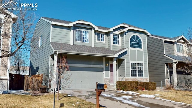 traditional-style home featuring roof with shingles, an attached garage, fence, stone siding, and driveway