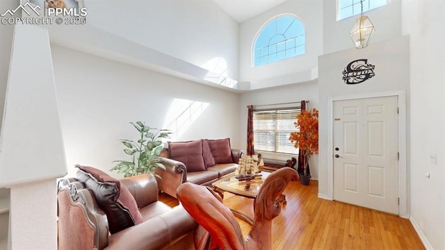 living room with a towering ceiling, light wood-style flooring, and baseboards