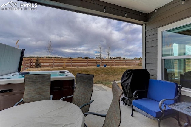 view of patio / terrace with outdoor dining space, a fenced backyard, a hot tub, and a rural view