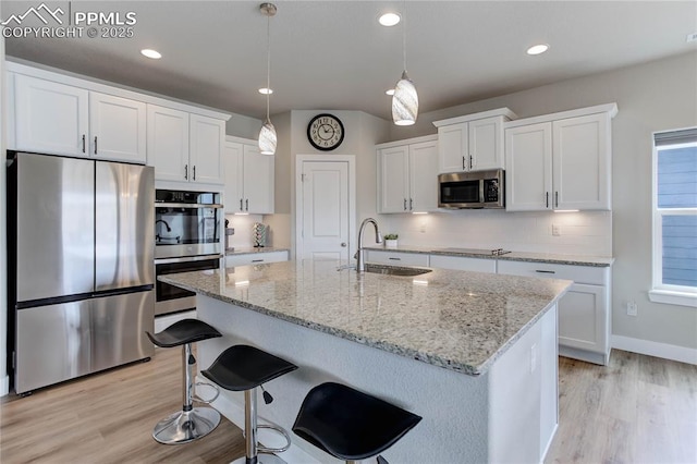 kitchen with stainless steel appliances, a sink, light wood-style floors, white cabinets, and tasteful backsplash