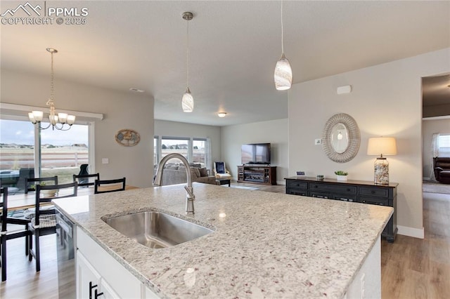 kitchen with light wood-style floors, white cabinets, a sink, and hanging light fixtures