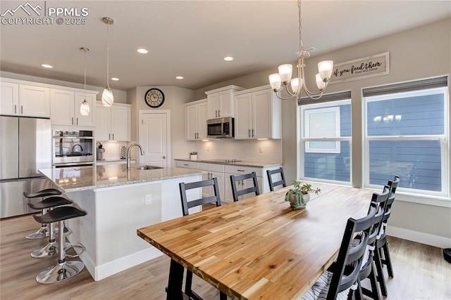 kitchen featuring stainless steel appliances, white cabinetry, light wood-style floors, tasteful backsplash, and a kitchen bar