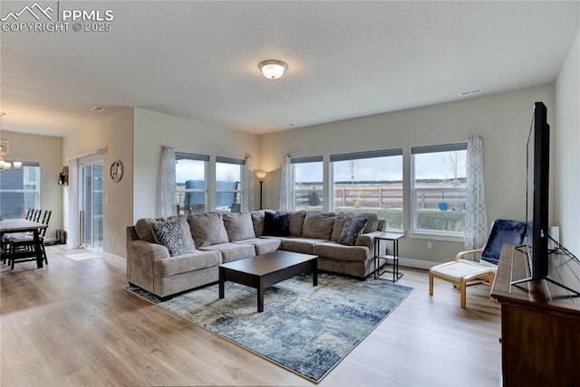 living room featuring a chandelier, baseboards, a textured ceiling, and light wood finished floors