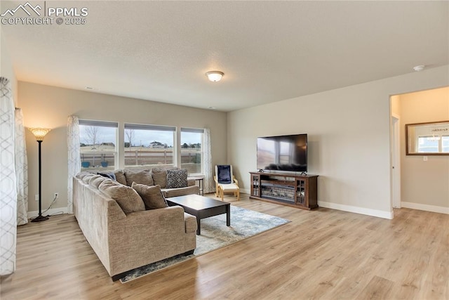 living room with baseboards, a textured ceiling, and light wood-style floors