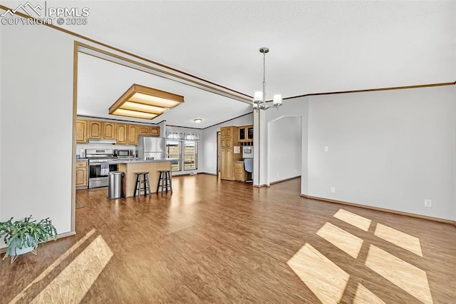 unfurnished living room featuring ornamental molding, an inviting chandelier, baseboards, and wood finished floors