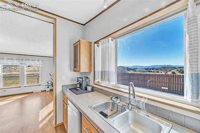 kitchen featuring crown molding, light countertops, glass insert cabinets, a sink, and dishwasher