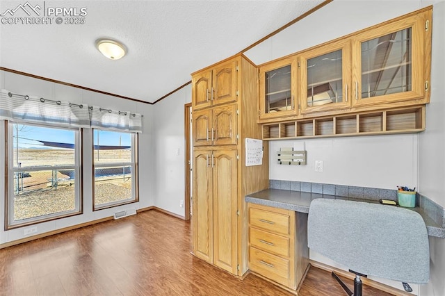 office featuring lofted ceiling, wood finished floors, visible vents, ornamental molding, and built in study area