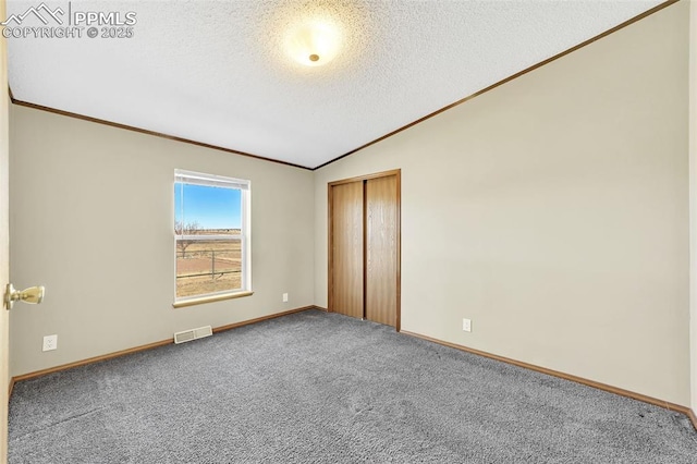 unfurnished bedroom with visible vents, lofted ceiling, ornamental molding, a textured ceiling, and carpet floors