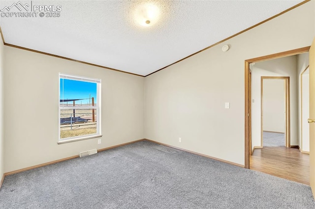 carpeted empty room featuring visible vents, crown molding, a textured ceiling, and baseboards