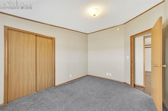 unfurnished bedroom with baseboards, carpet, a textured ceiling, crown molding, and a closet