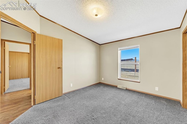 empty room featuring crown molding, visible vents, vaulted ceiling, and a textured ceiling