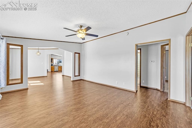 unfurnished living room with arched walkways, ornamental molding, a ceiling fan, a textured ceiling, and wood finished floors