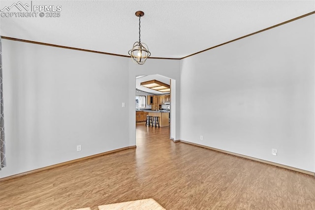 unfurnished room featuring baseboards, arched walkways, ornamental molding, wood finished floors, and a textured ceiling