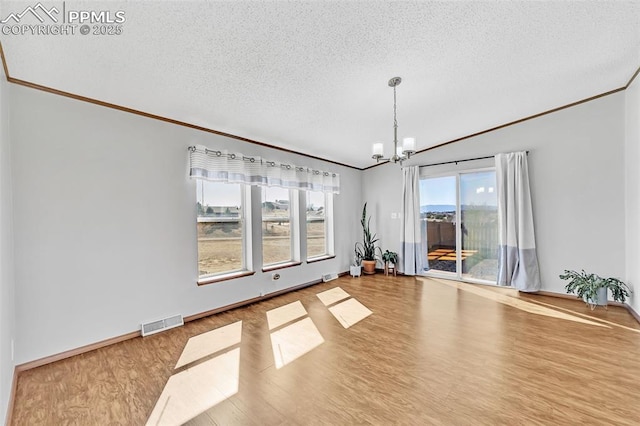 empty room with visible vents, a textured ceiling, an inviting chandelier, and wood finished floors