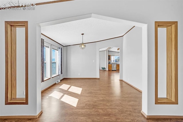 unfurnished room with arched walkways, visible vents, a textured ceiling, wood finished floors, and baseboards