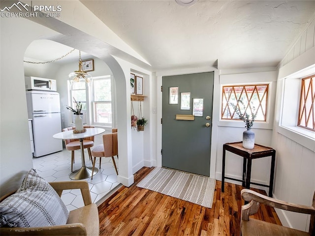 entrance foyer featuring arched walkways, wood finished floors, lofted ceiling, and an inviting chandelier