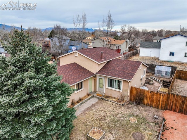 view of front of home featuring fence, roof with shingles, a residential view, stucco siding, and a mountain view