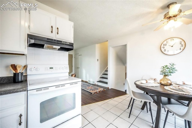 kitchen with under cabinet range hood, electric stove, light tile patterned flooring, white cabinets, and a textured ceiling