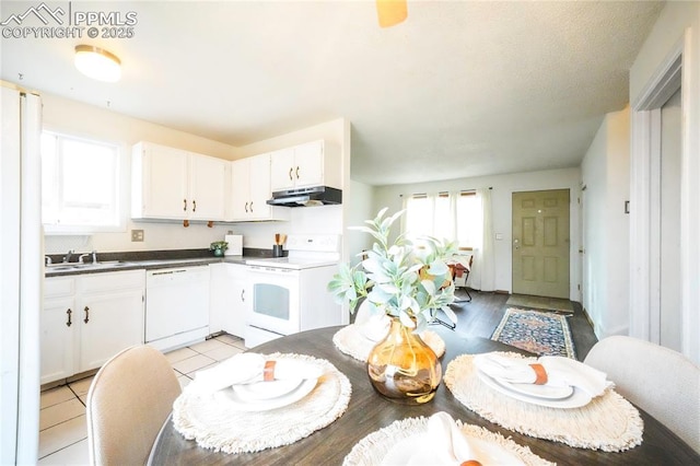 kitchen featuring under cabinet range hood, light tile patterned floors, white appliances, white cabinetry, and a sink