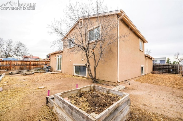 back of property featuring a fenced backyard, stucco siding, and a vegetable garden