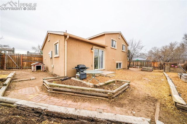 back of house featuring a vegetable garden, a fenced backyard, and stucco siding