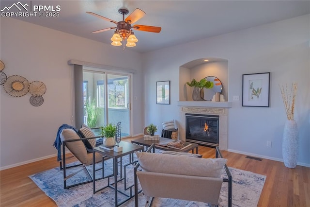 living room featuring a ceiling fan, baseboards, wood finished floors, and a glass covered fireplace