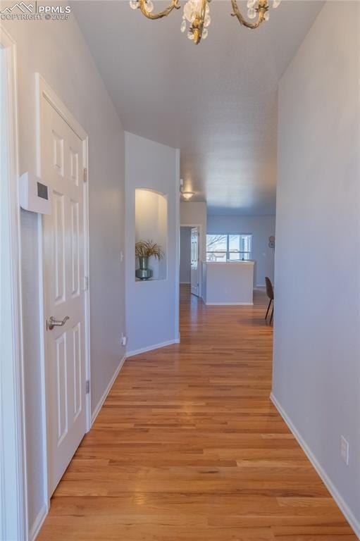 corridor featuring baseboards, light wood finished floors, and an inviting chandelier