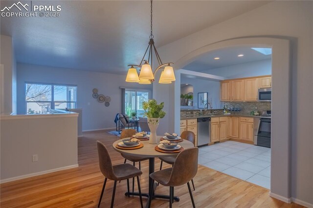 dining room with light wood-type flooring, a notable chandelier, lofted ceiling, and baseboards