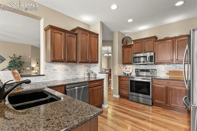 kitchen with light wood finished floors, tasteful backsplash, appliances with stainless steel finishes, a sink, and dark stone countertops