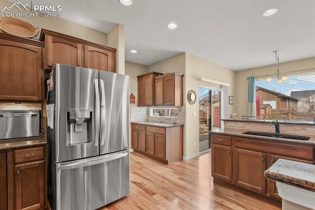 kitchen with light wood finished floors, dark stone countertops, a sink, stainless steel refrigerator with ice dispenser, and backsplash