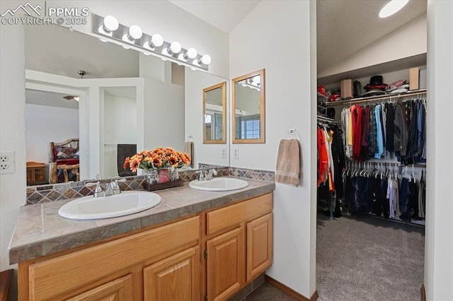 bathroom featuring double vanity, a spacious closet, vaulted ceiling, and a sink