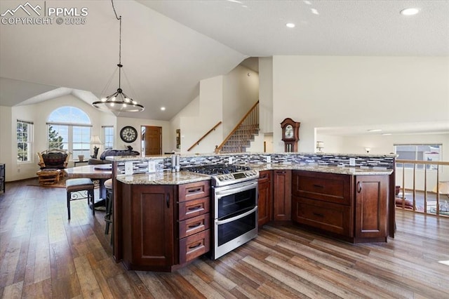 kitchen featuring range with two ovens, pendant lighting, wood finished floors, open floor plan, and light stone countertops