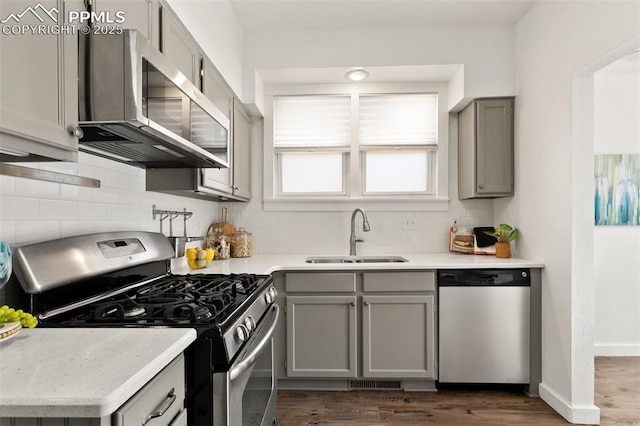 kitchen with dark wood-style flooring, a sink, appliances with stainless steel finishes, gray cabinets, and tasteful backsplash