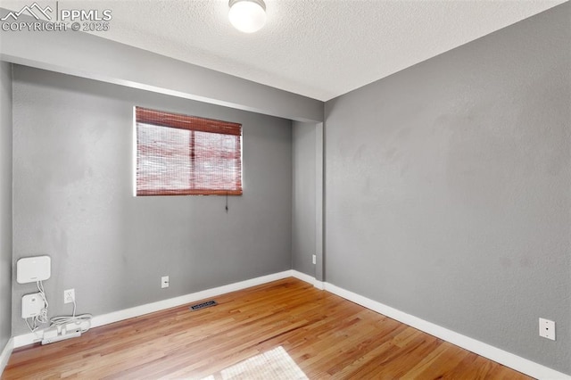 spare room with baseboards, a textured ceiling, visible vents, and wood finished floors