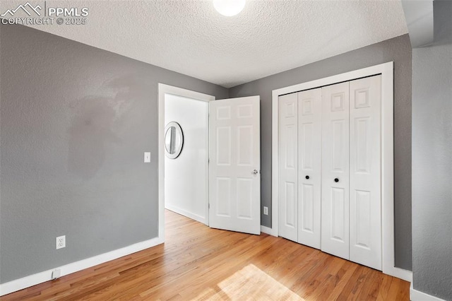 unfurnished bedroom with baseboards, a textured wall, wood finished floors, a textured ceiling, and a closet