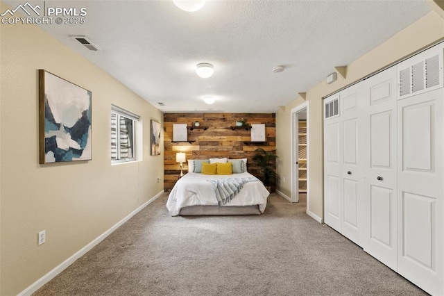 bedroom with a closet, visible vents, carpet flooring, wooden walls, and a textured ceiling