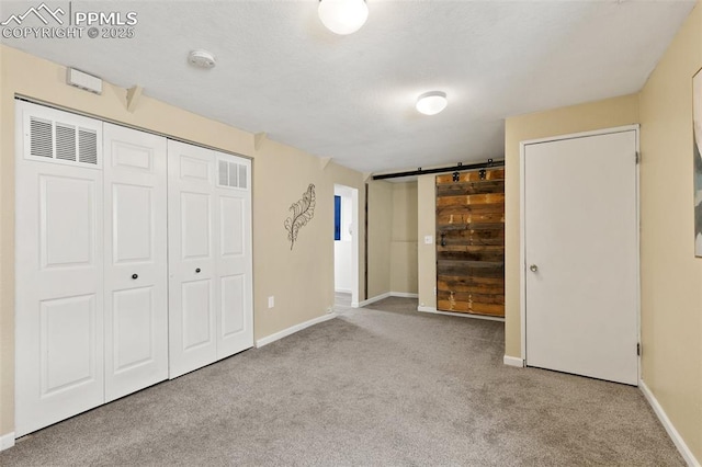 unfurnished bedroom with a barn door, baseboards, visible vents, carpet floors, and a closet