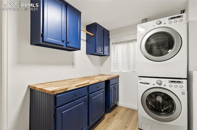 laundry area featuring cabinet space, light wood finished floors, and stacked washing maching and dryer