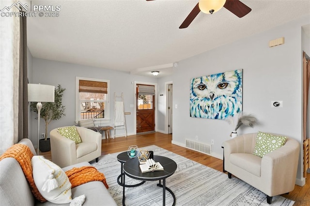 living room with visible vents, a textured ceiling, baseboards, and wood finished floors