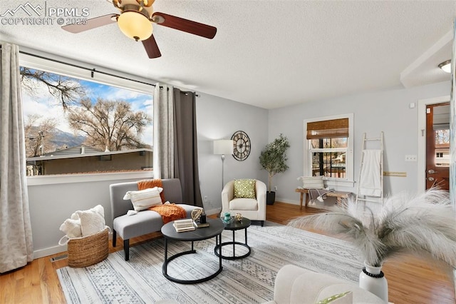 living area with a textured ceiling, wood finished floors, a wealth of natural light, and baseboards