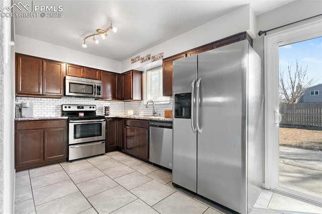 kitchen with a sink, stainless steel appliances, light stone countertops, and backsplash